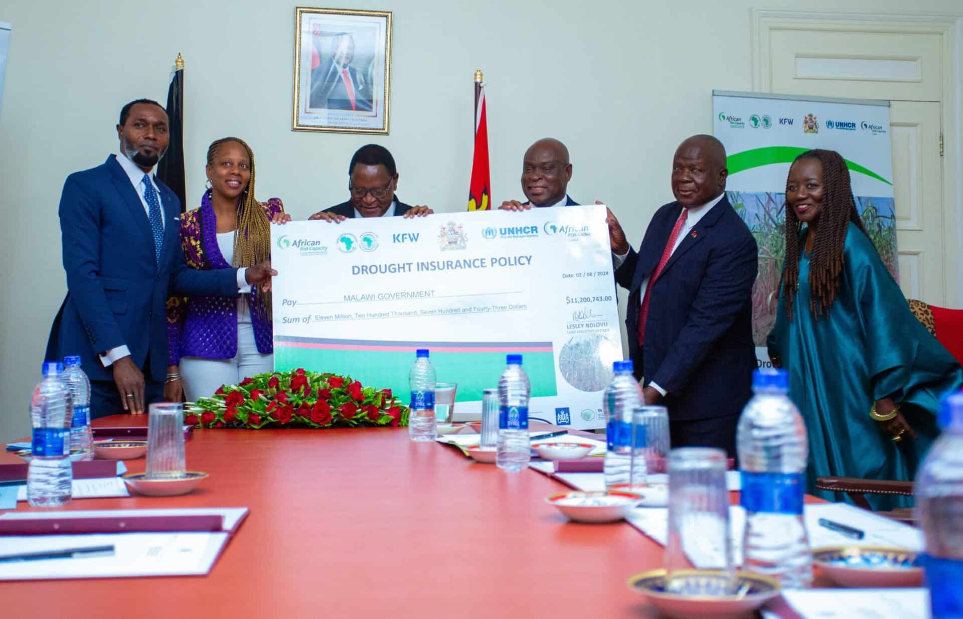 Malawi officials and UNHCR representatives display insurance payout check for drought relief.