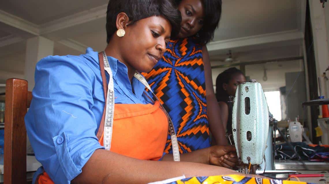 Young African woman sewing with mentor support.