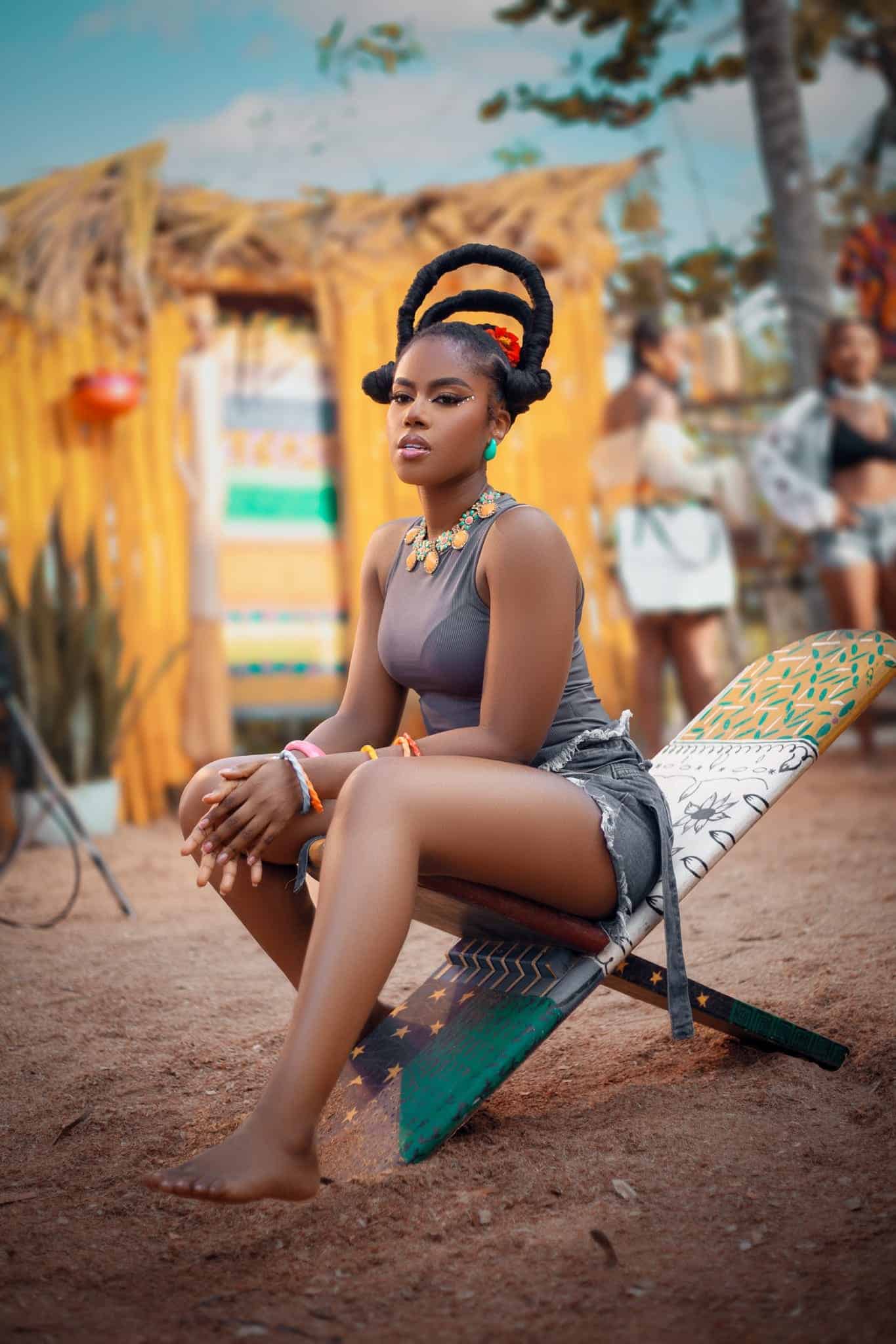 MzVee sitting on a beach chair with tropical background, enjoying the seaside.