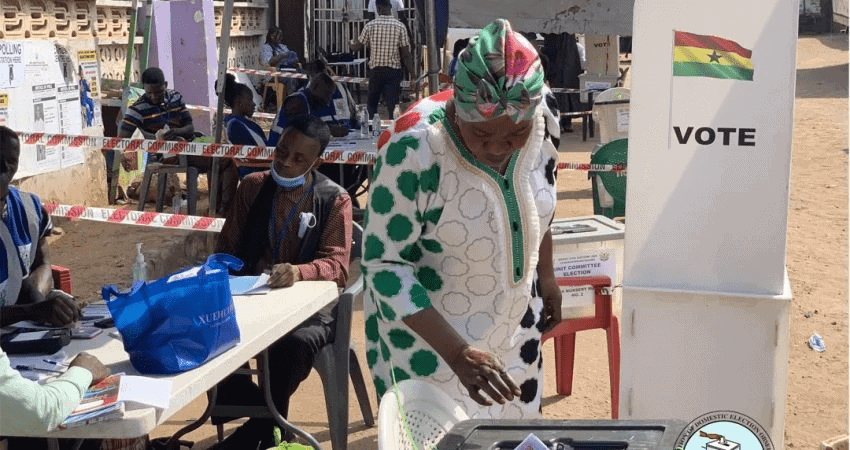 Voter casting ballot at polling station in Ghana during election process.
