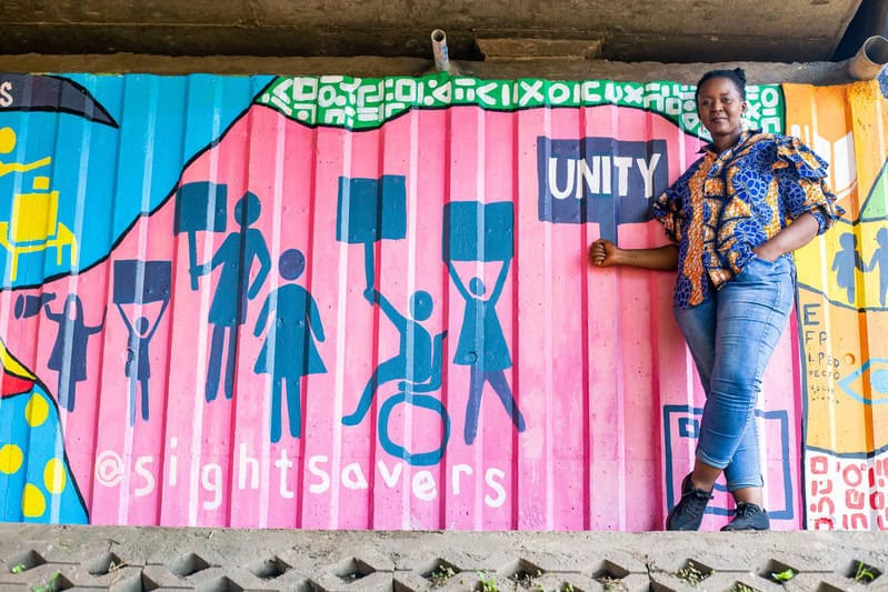 Woman standing next to a colorful mural promoting disability inclusion and unity.