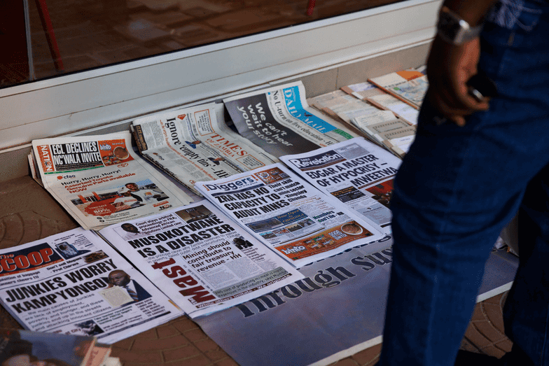 Journalist standing near newspapers highlighting press freedom issues in Zambia.
