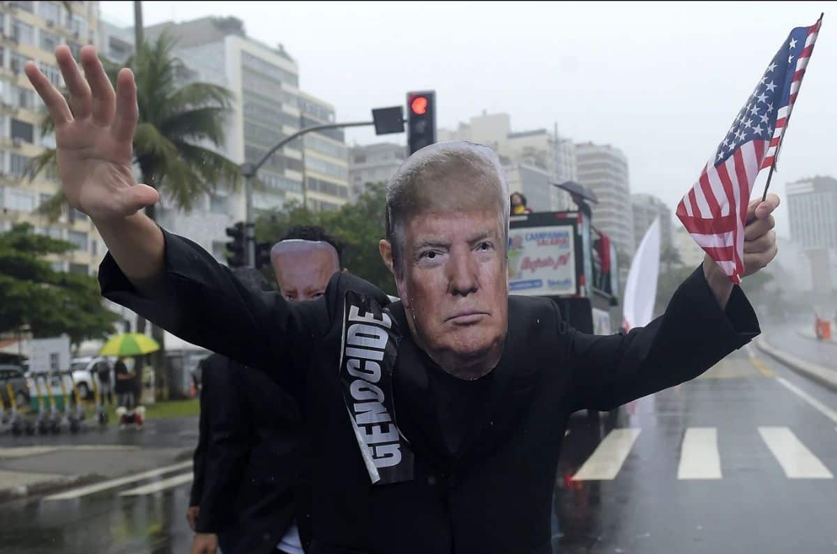Man holding American flag during a protest in a city street with tall buildings and palm trees.