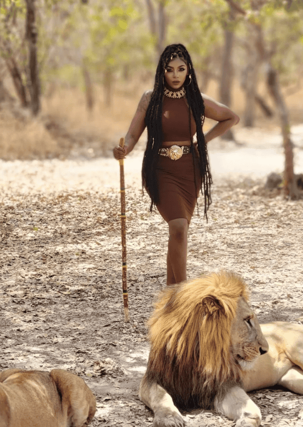Woman in traditional attire with lion in a savannah setting.