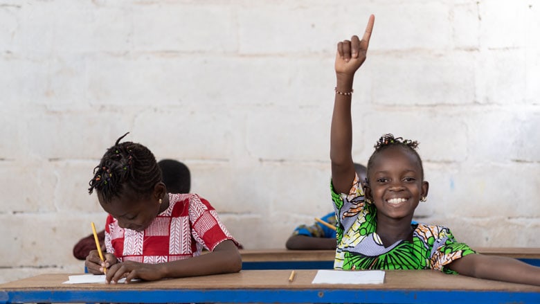 Happy African girl raising hand in classroom with classmates.