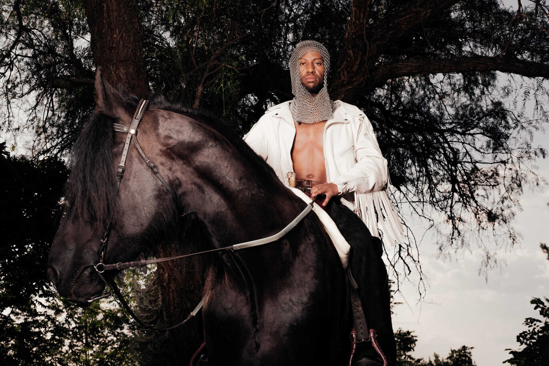 Moonga K. riding a black horse outdoors with trees in the background.