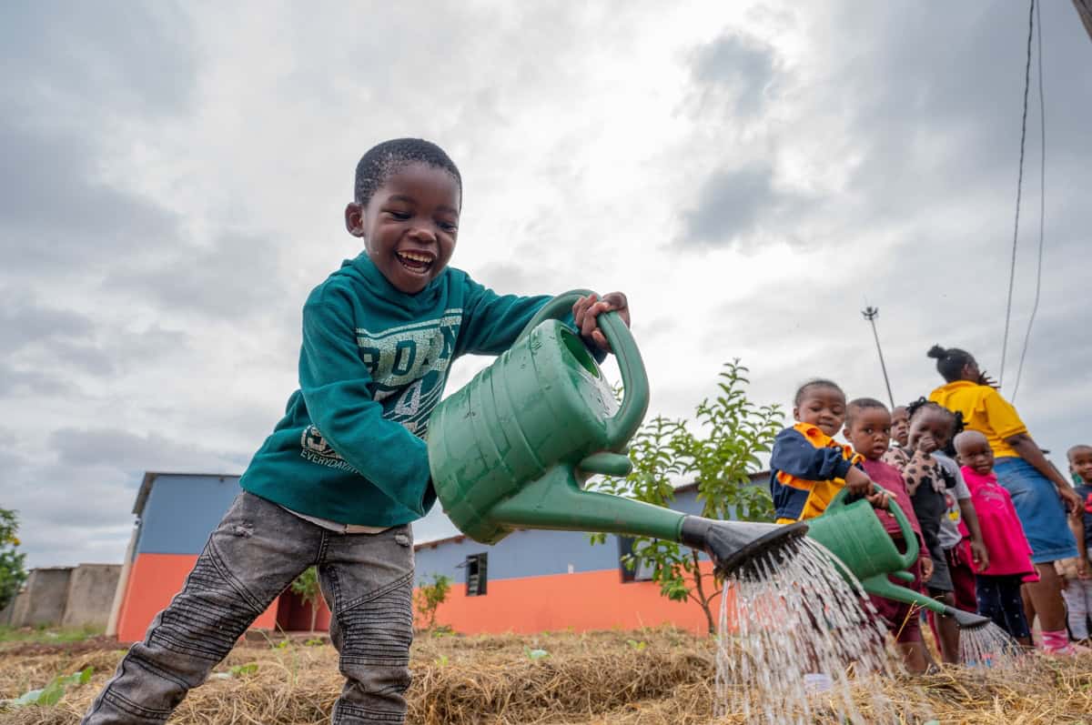 Young child watering plants at climate-resilient early learning center.