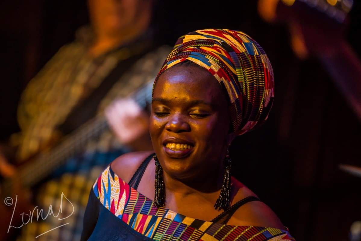 African woman in traditional attire performing at a music event.