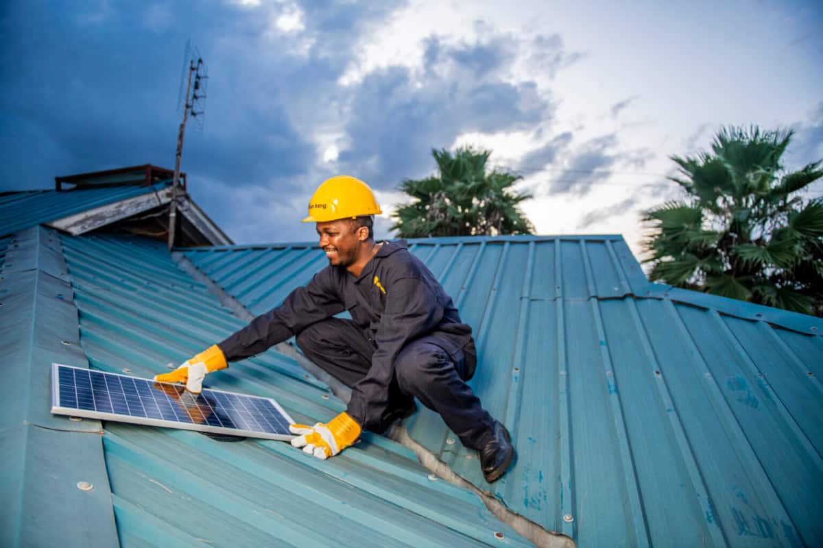 Solar panel installation worker installing solar panels on a blue roof in Kenya.