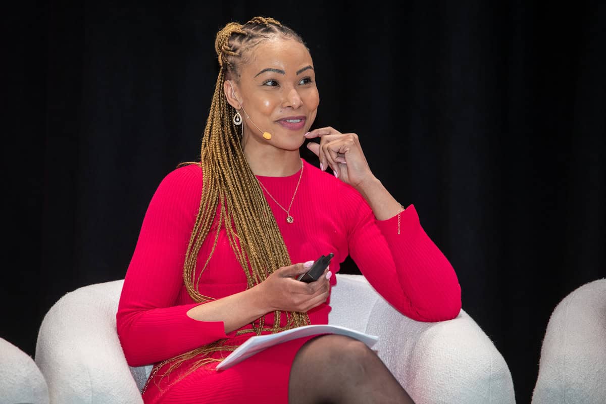 South African woman speaker at conference, wearing red dress, holding microphone, discussing women’s.