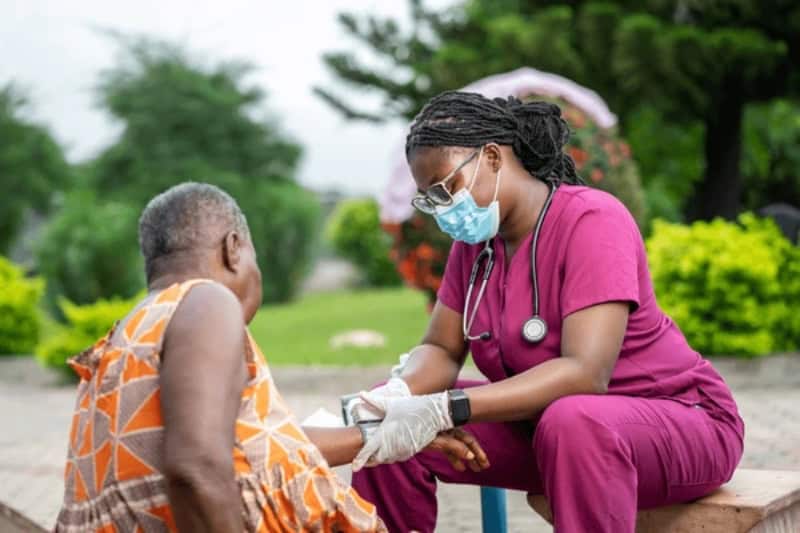 Healthcare worker providing medical care to elderly woman outdoors.