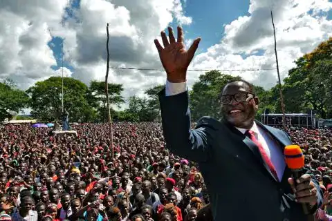Malawi political rally with a speaker addressing a large crowd outdoors.