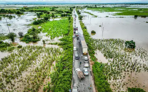 Flooded road with vehicles navigating through water in Southern Africa.