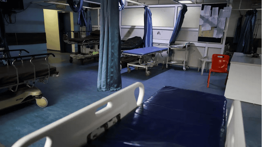 Empty hospital bed with curtains in a busy medical ward.
