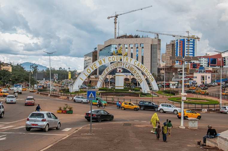 Cameroon cityscape with ongoing construction, traffic, and a prominent arch reading "Love My Country.