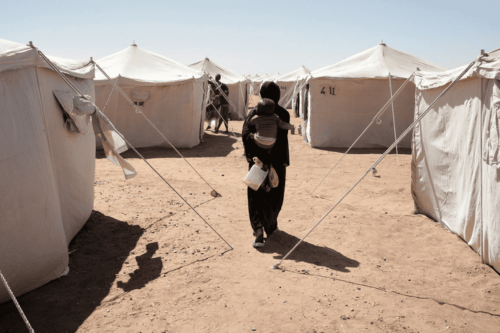 Refugee woman walking through tents in Darfur displacement camp.