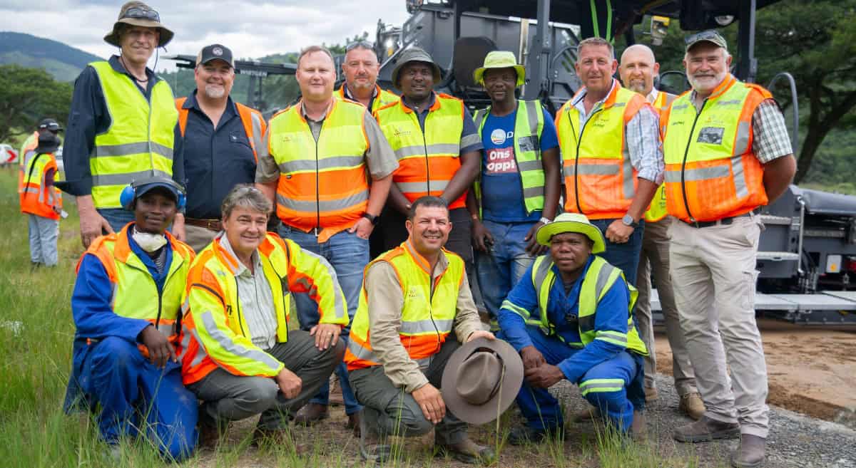 Group of engineers and workers in high-visibility vests at road recycling site.