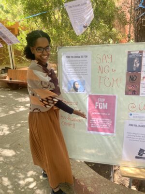 African woman standing next to a display board with posters on digital rights and equality.