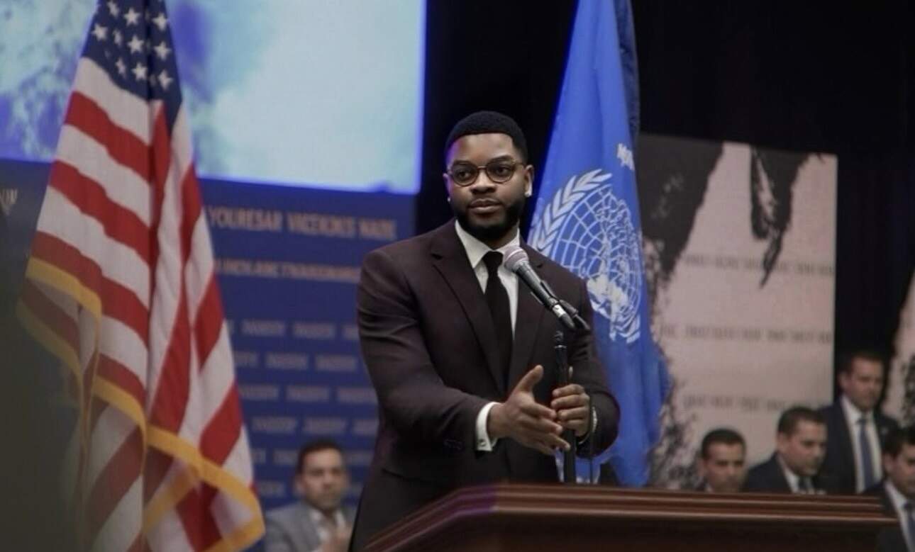 African diplomat speaking at international conference with UN flag in background.
