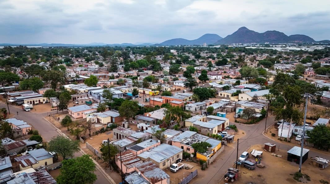 Aerial view of a Botswana village showing houses, roads, and greenery with mountains in the distance.