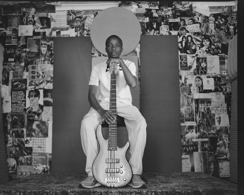 Young jazz artist holding bass guitar in vibrant Cape Town street scene.
