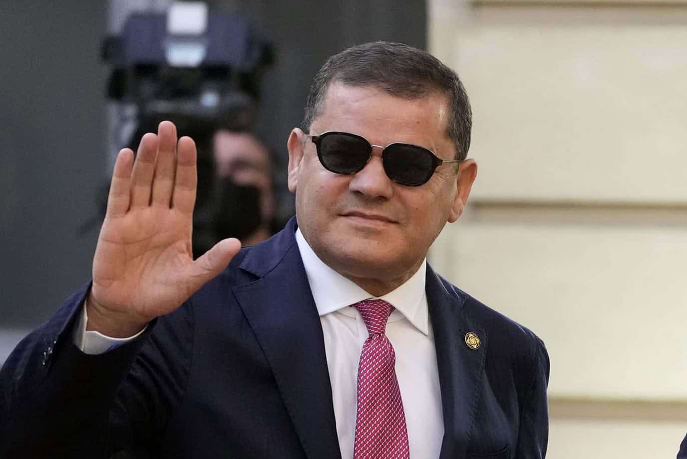 Prime Minister of Libya waving, wearing sunglasses, and formal attire.