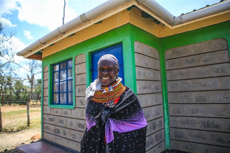 Empowered woman standing outside a new, colorful house in Africa.
