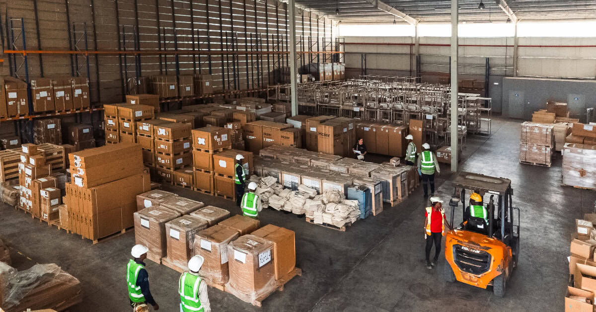 Warehouse workers managing packages with forklift in an industrial storage facility.