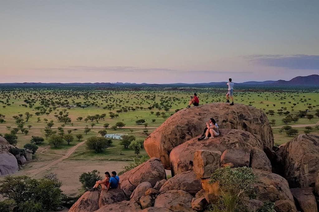 People enjoying panoramic view from large rocks in African landscape.