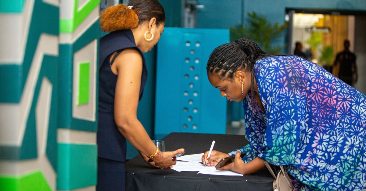 Two women signing documents at a registration desk in an office setting.