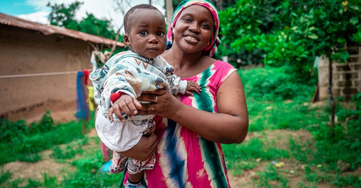 Mother holding her child outdoors in a rural setting, symbolizing global health initiatives.
