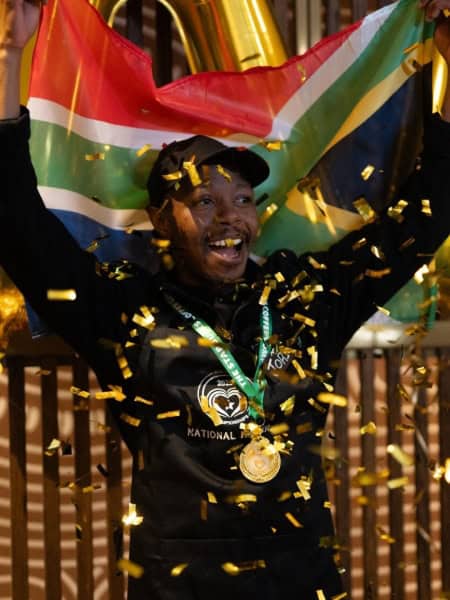 African barista celebrating victory with flag and medals.