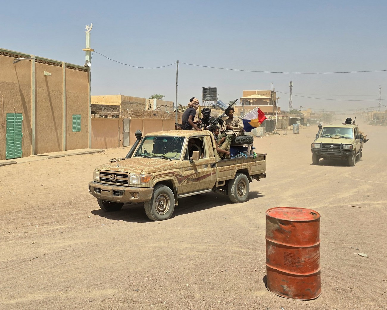 Military vehicle with soldiers riding through a dusty African town street.