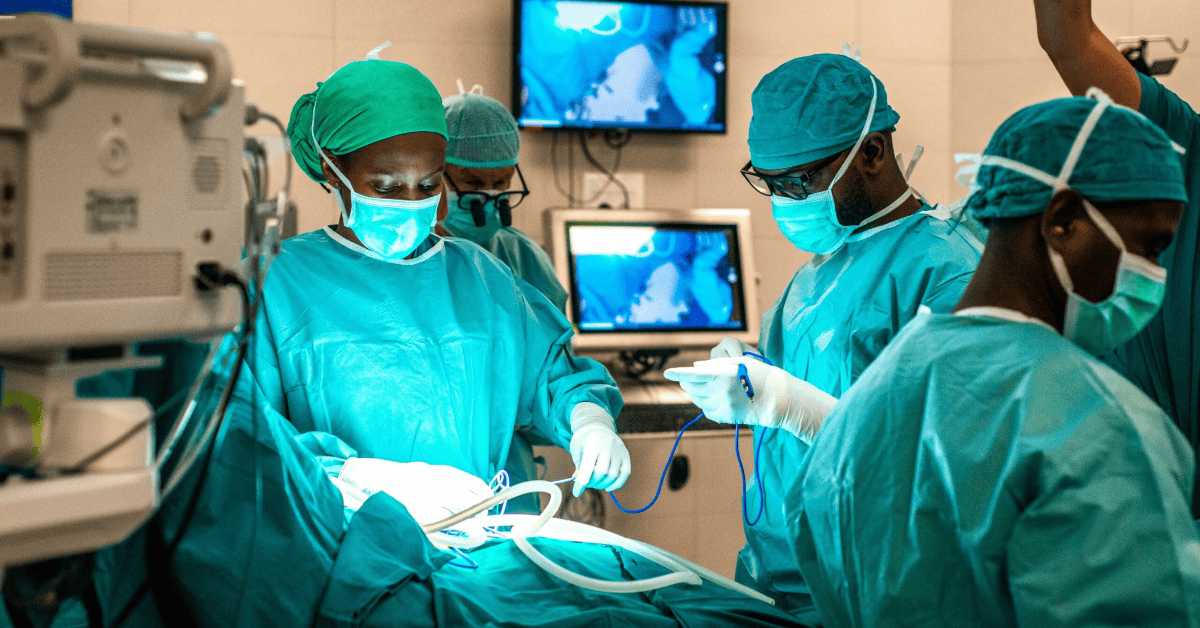 Medical team in surgery room with healthcare professionals in scrubs and masks.