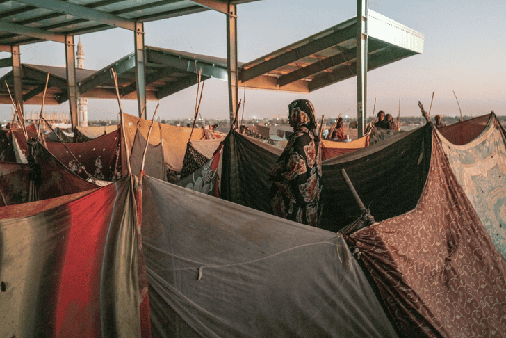Refugees in a camp with tents and makeshift shelters during sunset.