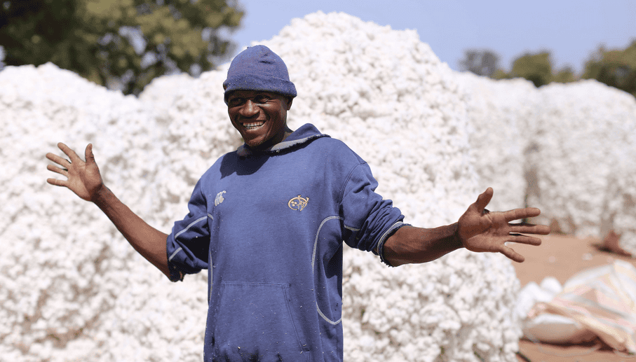 Happy cotton farmer in Burkina Faso with cotton bales in the background.