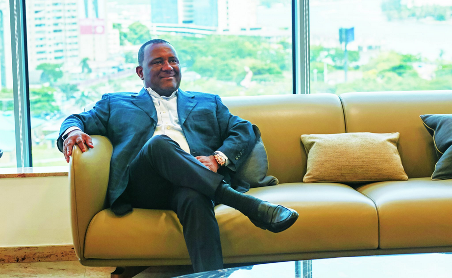Nigerian billionaire sitting on a sofa in a modern office setting.