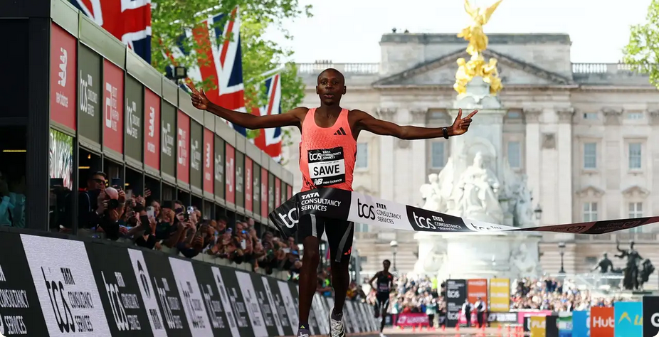 African runner crossing finish line at London Marathon, celebrating victory.