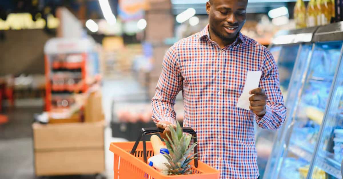 South African man shopping for fresh produce with a smartphone in a supermarket.