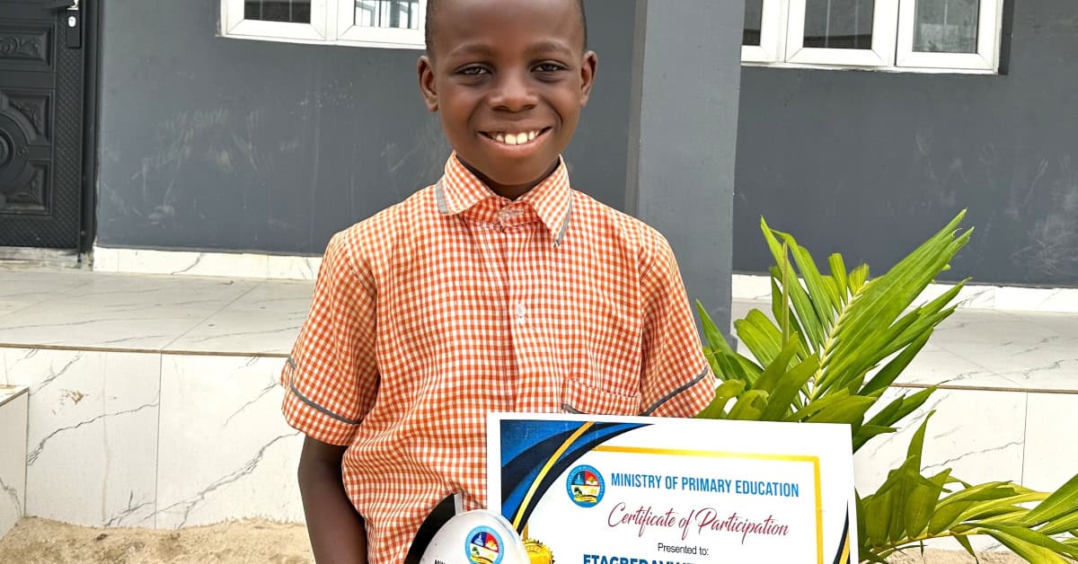 Young boy smiling with certificate of participation at Transcorp Power School.