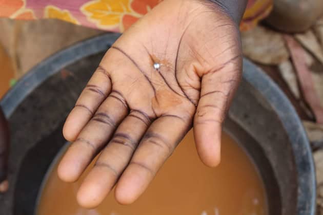 Hand holding mercury drop for gold extraction.