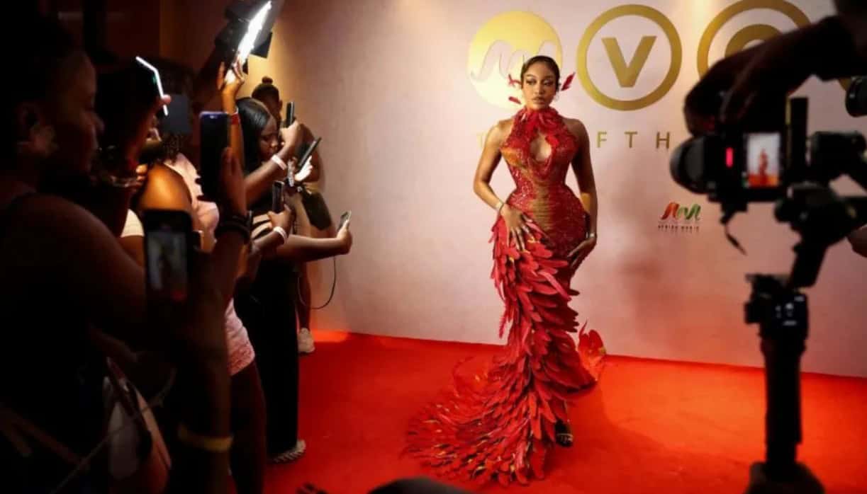 Elegant woman in striking red gown on the red carpet at African film awards event.