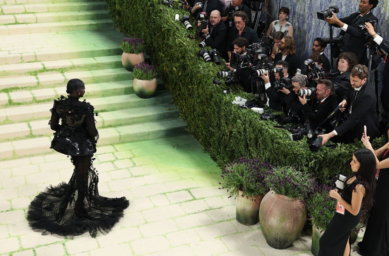 Elegant black gown showcased on runway with photographers capturing the moment.