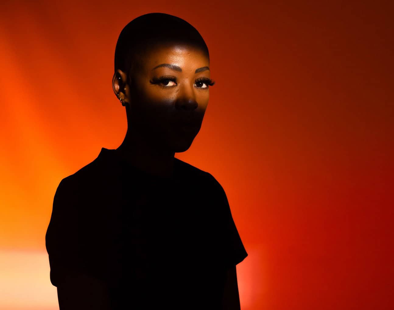 Stylish woman with short hair and makeup, illuminated by warm orange lighting, creating a striking s.