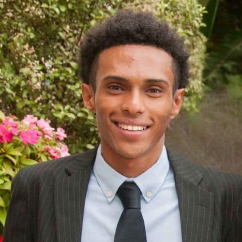 About Us 3 Young professional man smiling outdoors in a suit.