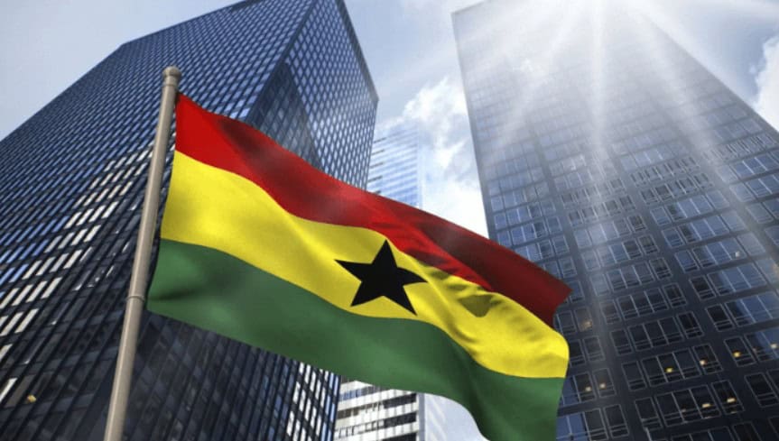 Ghana flag flying in front of tall modern office buildings in Accra.