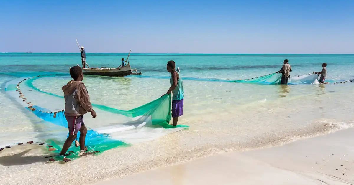 Fishing community on a tropical African beach, with locals casting nets into the clear blue sea.