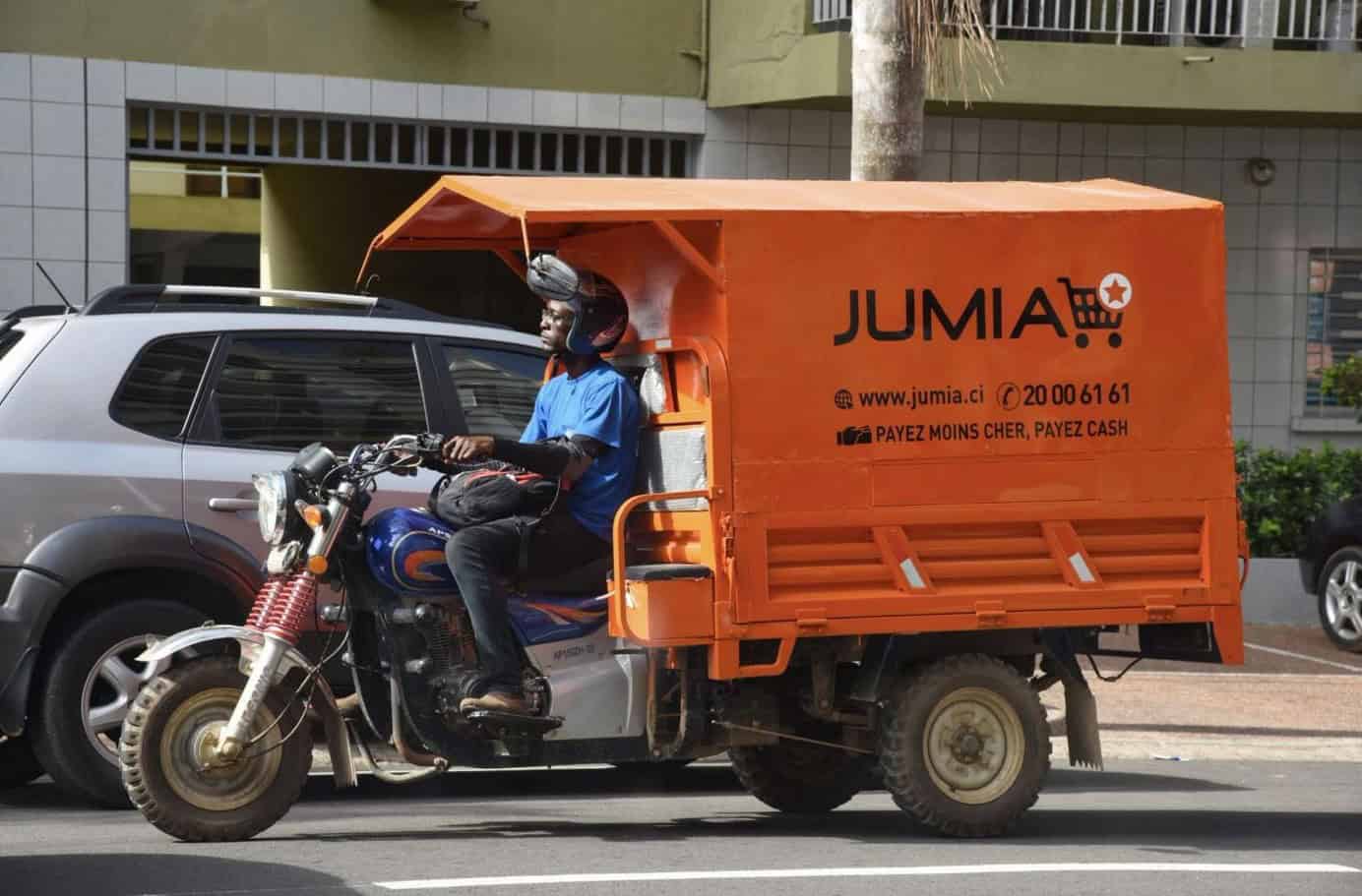Motorcycle delivery rider with Jumia cargo in an urban African setting.
