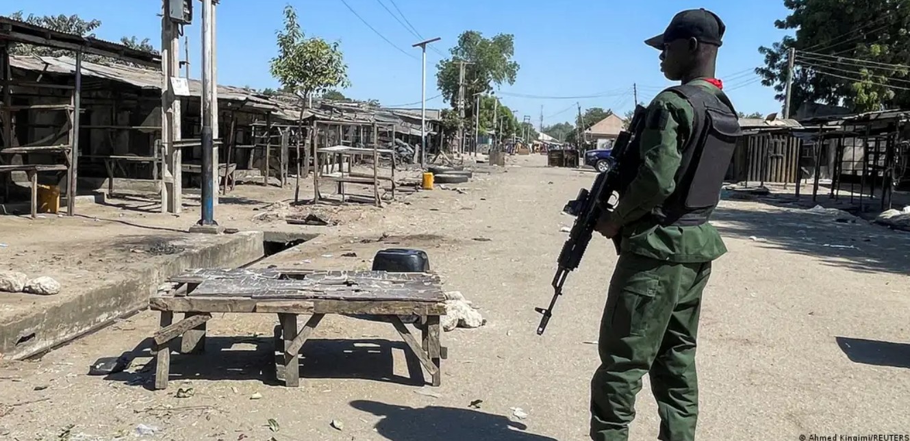 African security officer standing with rifle in a village setting.