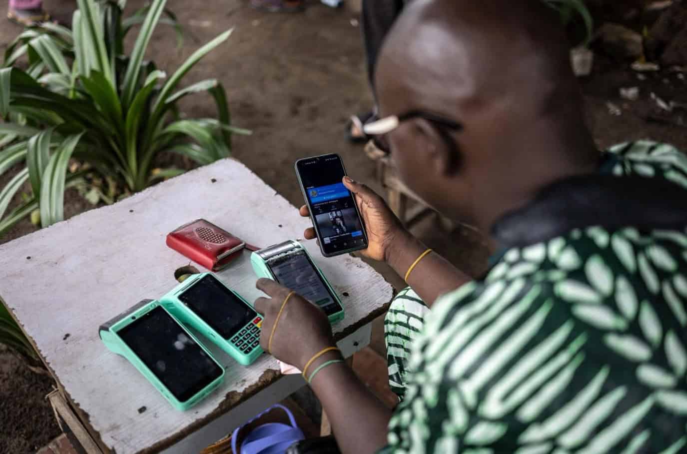 Mobile phones on a table with a person using one outdoors in Africa.